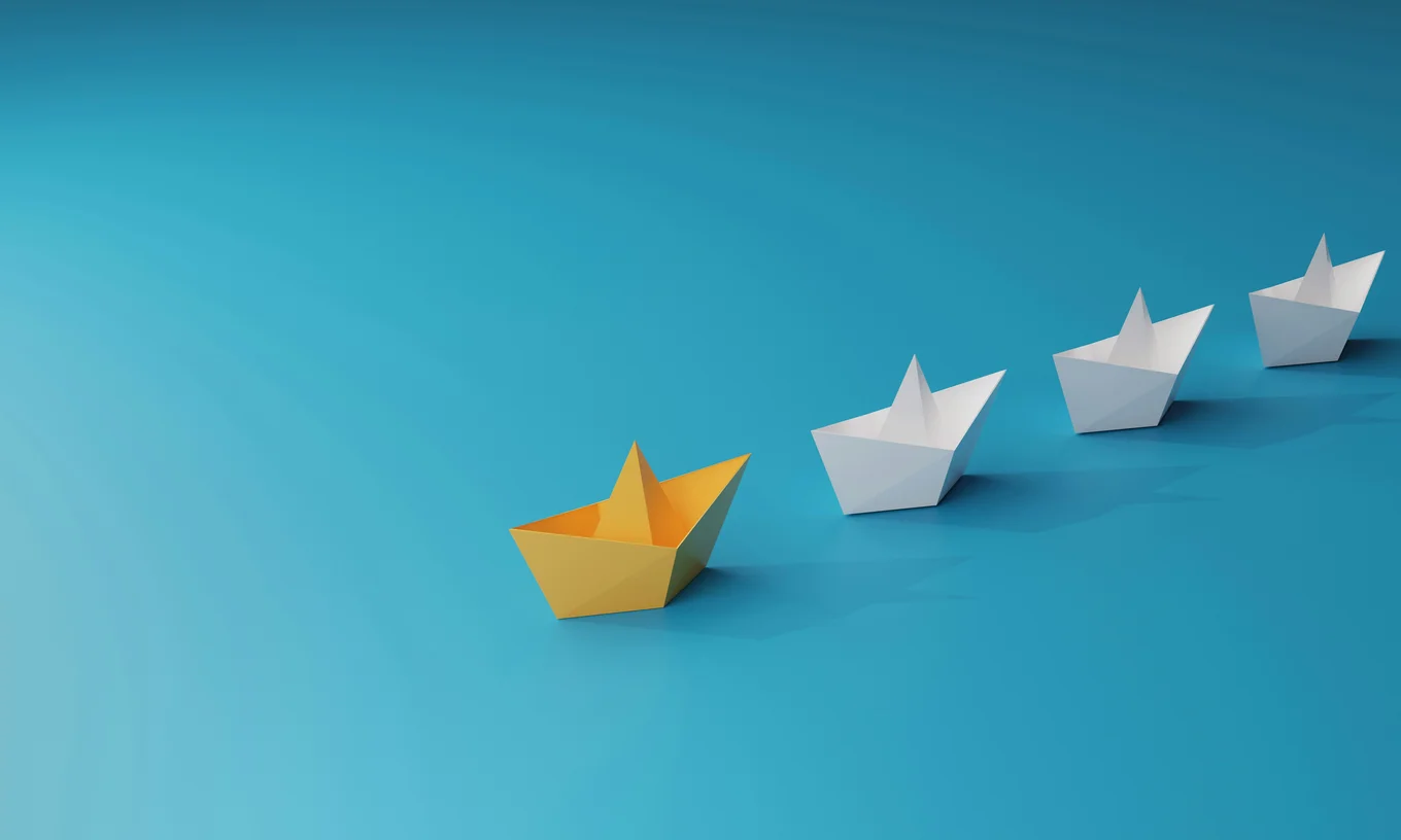 A 3d render of paper boats against a blue background. They are in a line from the centre of the image towards the top right. The first one is yellow and the three others are white.